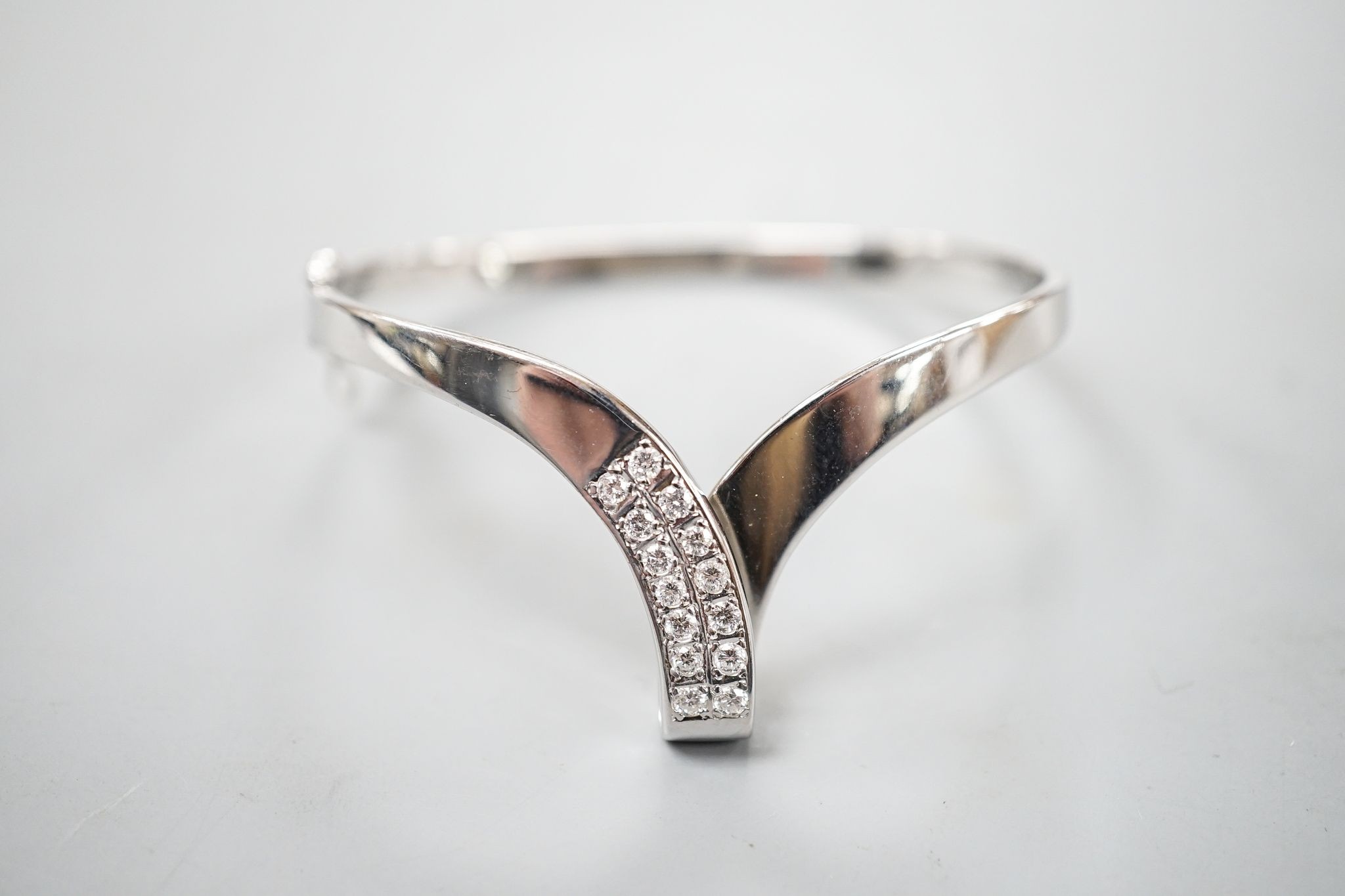 A modern 585 white metal and twelve stone diamond set wishbone shaped hinged bangle, gross 19.7 grams.